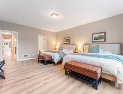 Luxury golf rental bedroom with two queen beds, ensuite bathroom access, and coastal artwork at Bandon Dunes vacation rental