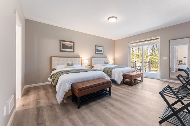 Spacious guest bedroom with two queen beds, patio access, and forest views at Bandon's Trail House