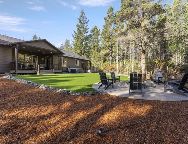 Exterior of Bandon's Trail House with fire pit, lawn, and forest setting on wooded property